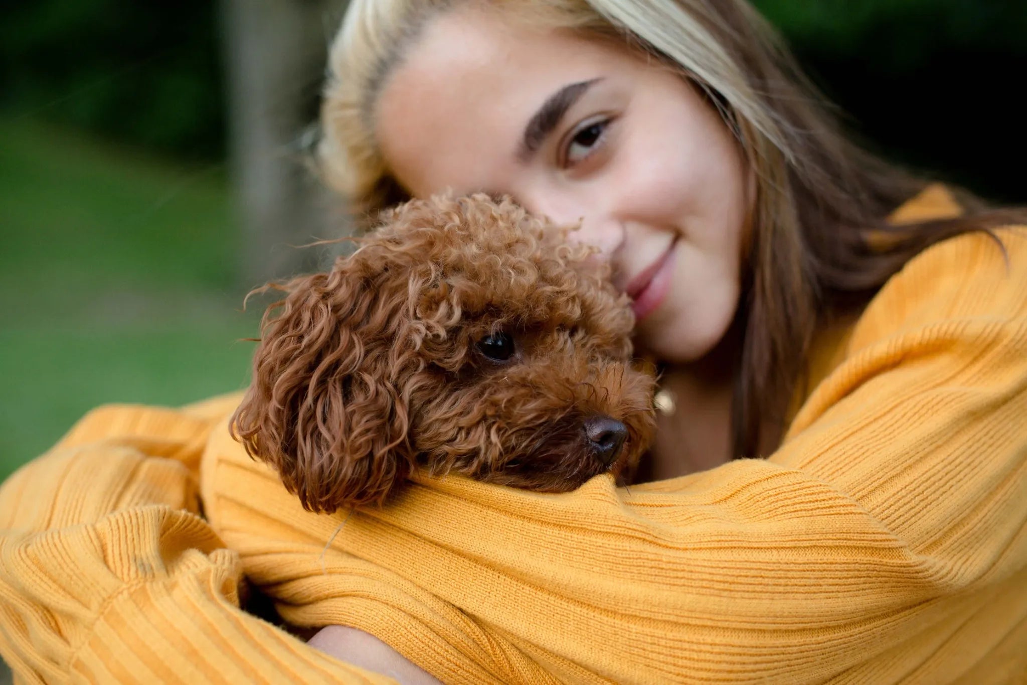 Sharrets pet wellness – woman in yellow sweater hugging a cute brown dog, promoting love and healthy living for pets.