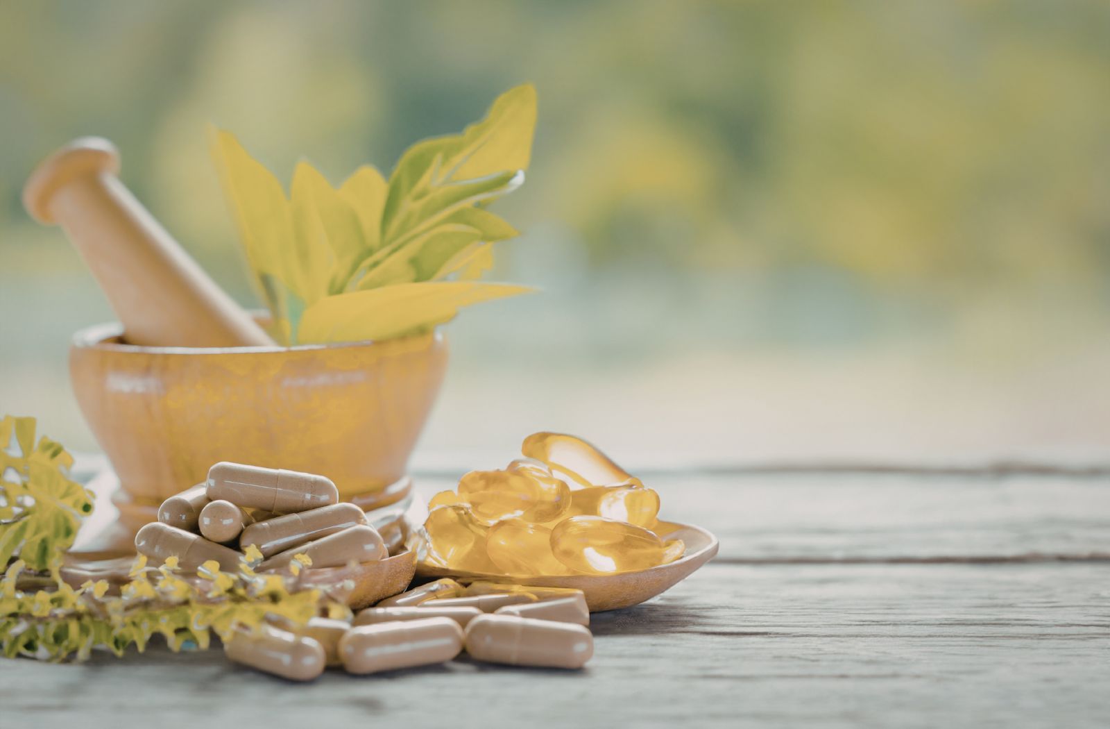 Supplements including capsules and pills on a wooden surface with a mortar and pestle.